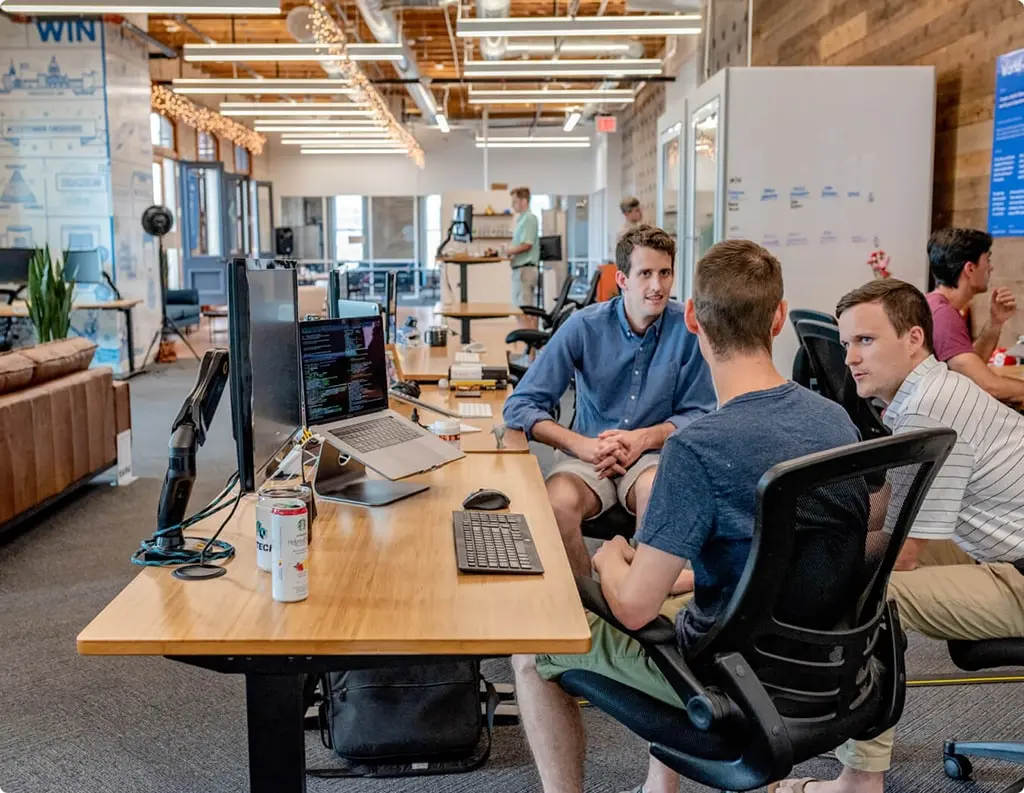 Three colleagues engaged in a discussion at a workstation in a modern office environment.