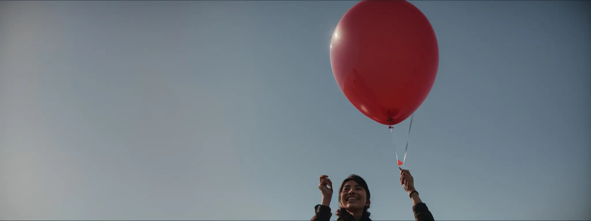 a smiling person holding a five-star shaped balloon against a bright, sunny sky.