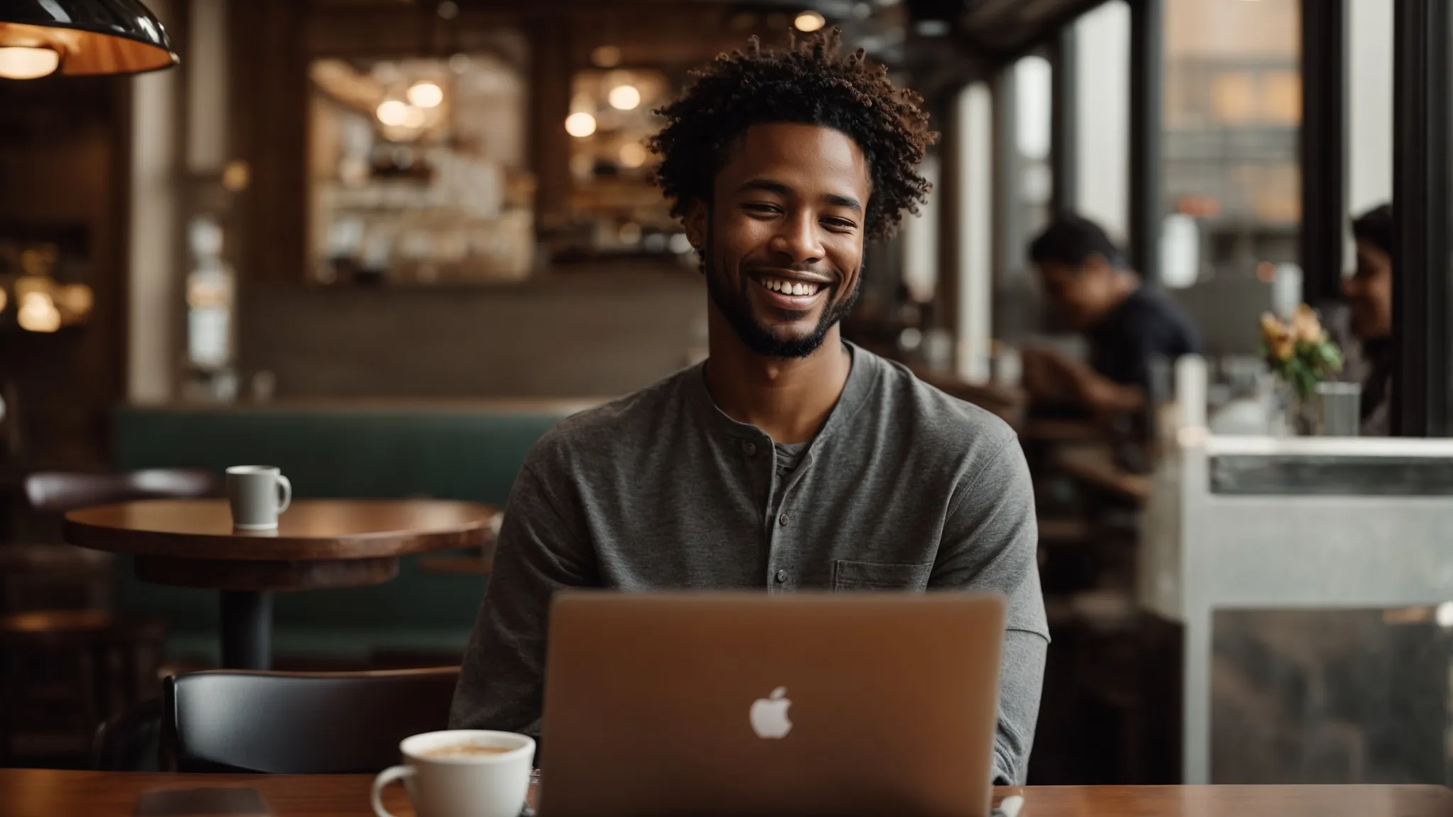 a customer smiling while using a laptop at a cozy coffee shop table.