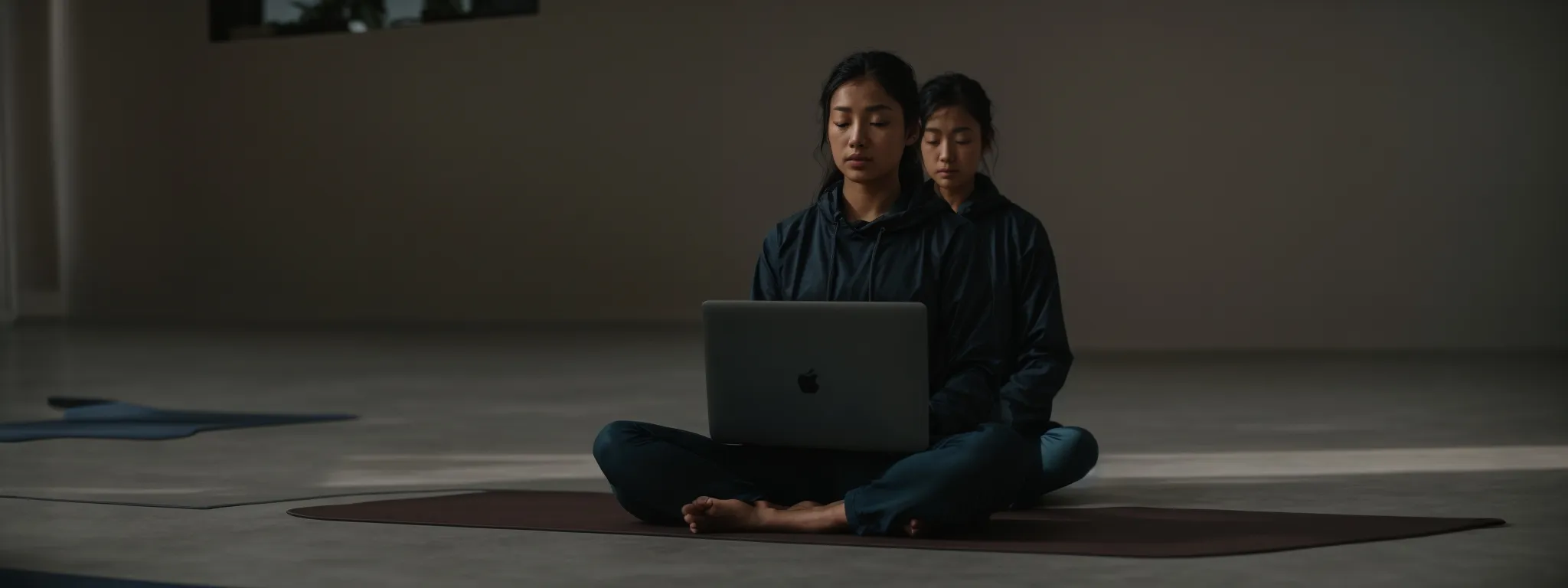 a yoga instructor sitting cross-legged with a laptop on a mat, immersed in research.