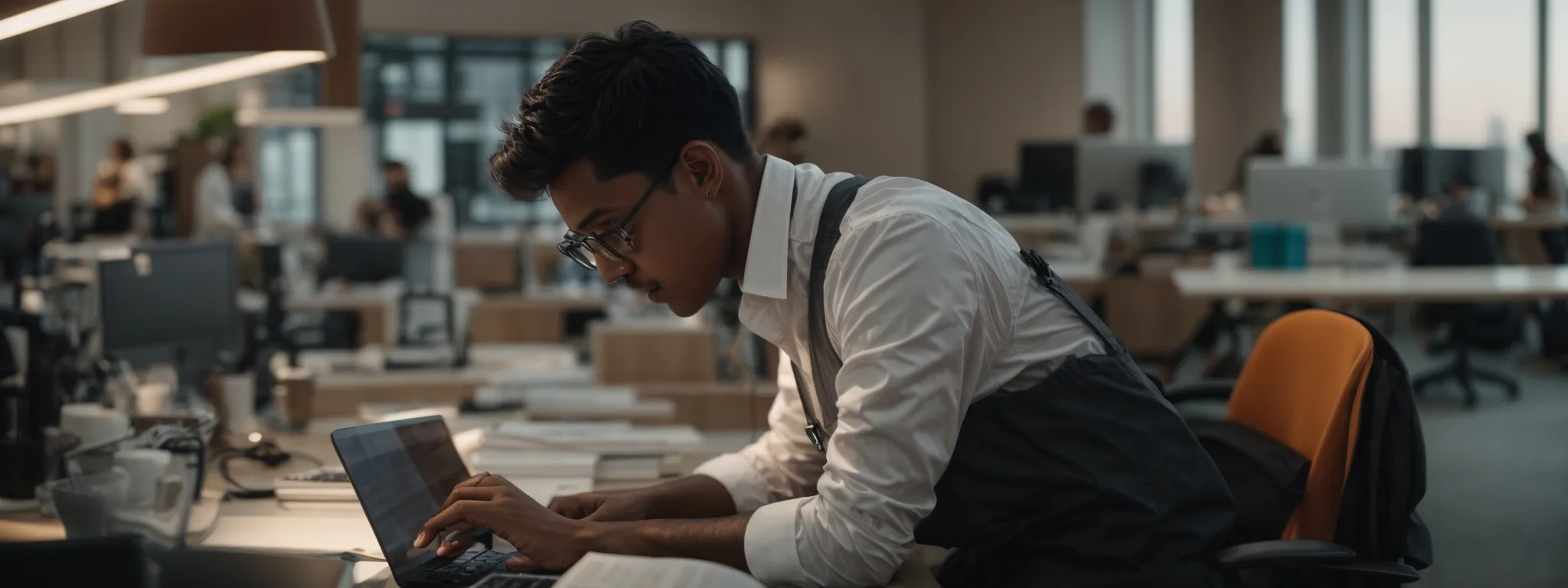 a focused individual working on a laptop in a bright, modern office space surrounded by technology and open books.