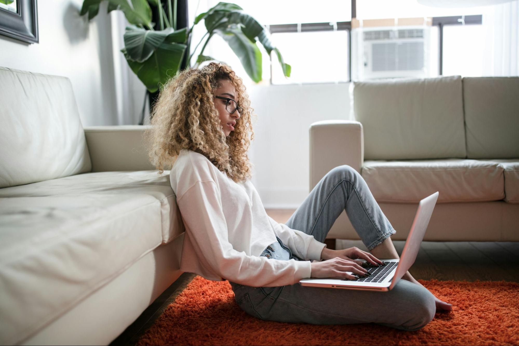 A person sitting on the floor with a laptop, researching options for an SEO outsourcing company or freelancer.