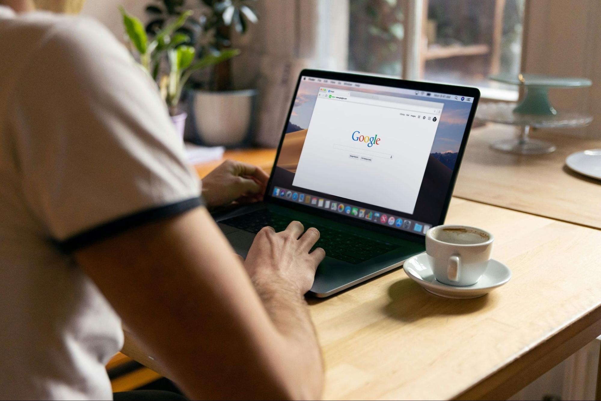 Person using Google search on a laptop with a coffee nearby, highlighting the importance of following Google's E-E-A-T guidelines to enhance visibility and credibility online